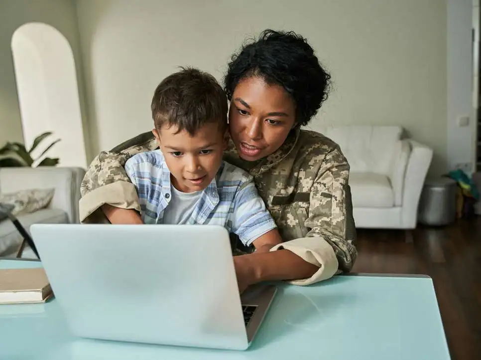 A woman and a child on her lap are typing on a laptop at a table.