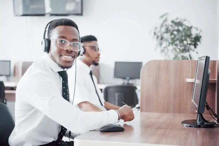 a man is wearing headphones and sitting at a desk with a computer in an office.